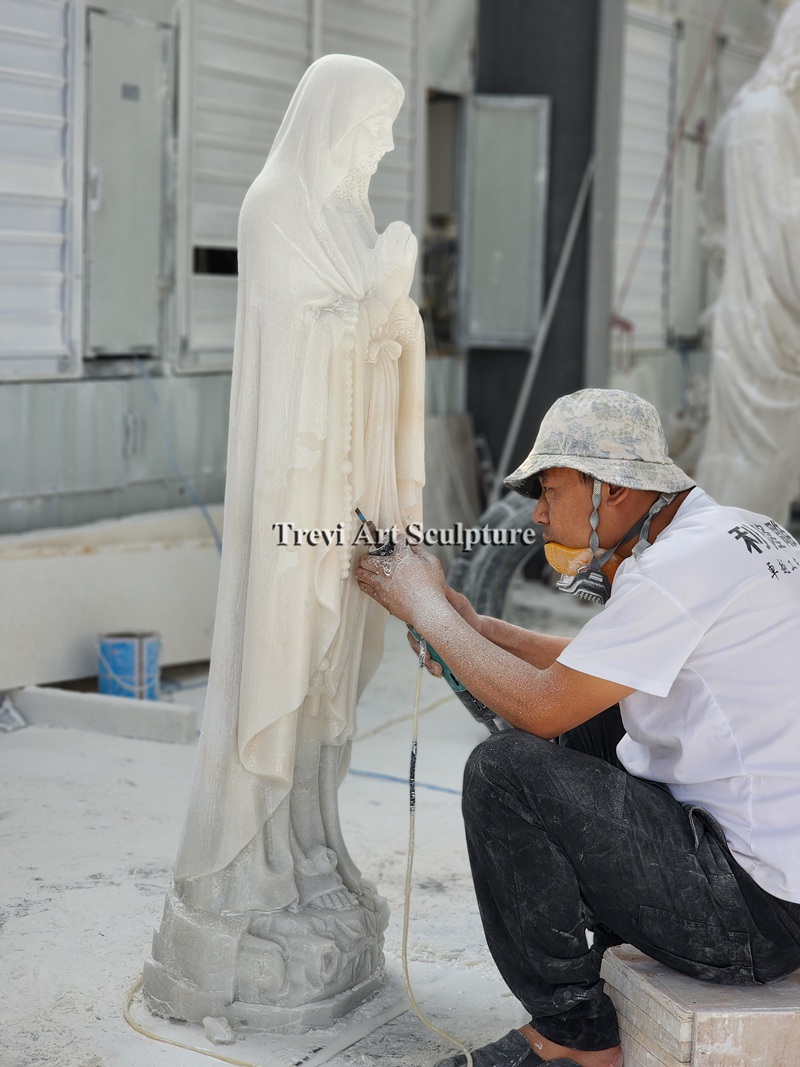 Finely shaping the folds of a white marble Mary statue
