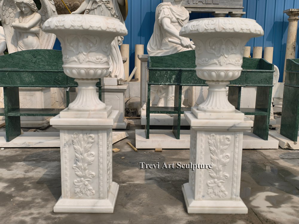 pair of ornate white marble planter urns set on matching relief carved pedestals
